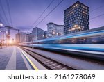 High speed train in motion on the railway station at sunset. Moving blue modern intercity passenger train, railway platform, buildings, city lights. Railroad in Vienna, Austria. Railway transportation