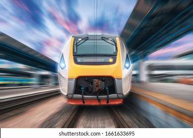 High speed train in motion on the railway station at sunset. Fast moving modern passenger train on the railway platform. Railroad with motion blur effect. Commercial transportation. Front view