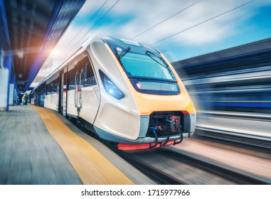 High speed train in motion on the railway station at sunset. Modern intercity passenger train with motion blur effect on the railway platform. Industrial. Railroad in Europe. Commercial transportation