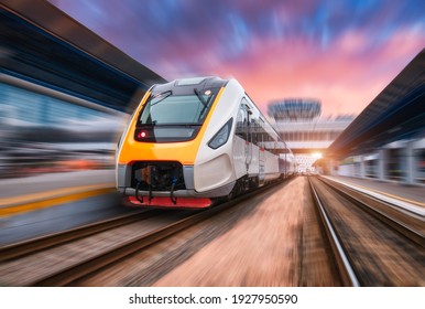 Hochgeschwindigkeitszug in Bewegung auf dem Bahnhof bei Sonnenuntergang. Schnell fahrender moderner Personenzug auf Bahnsteig. Eisenbahn mit unscharfem Bewegungseffekt. Gewerblicher Transport. Vorderseite. Konzept
