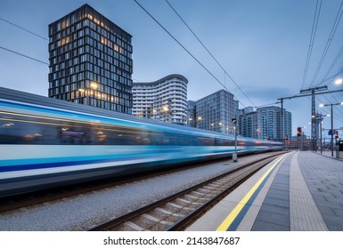 High speed train in motion on the railway station at dusk. Moving blue modern intercity passenger train, railway platform, buildings, city lights. Railroad in Vienna, Austria. Railway transportation