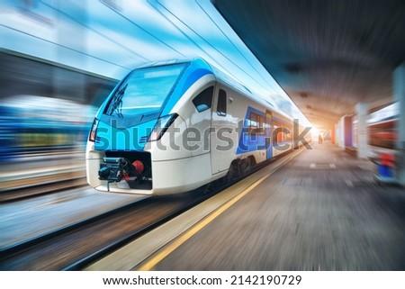 High speed train in motion on the railway station at sunset. Blue modern intercity passenger train with motion blur effect on the railway platform. Railroad in Europe. Commercial transportation