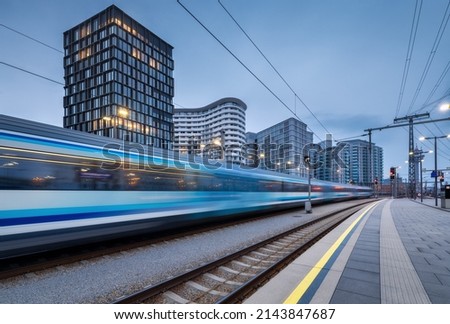 High speed train in motion on the railway station at dusk. Moving blue modern intercity passenger train, railway platform, buildings, city lights. Railroad in Vienna, Austria. Railway transportation