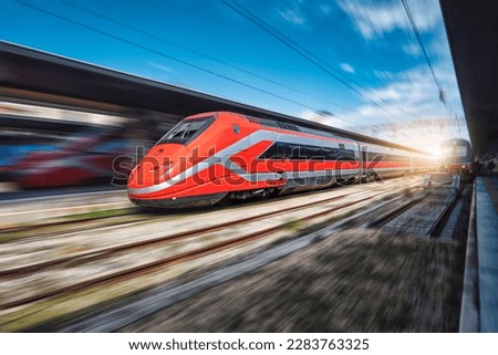 High speed train in motion on the railway station at sunset. Fast red modern intercity train and blurred background. Railway platform. Railroad in Italy. Commercial. Passenger railway transportation