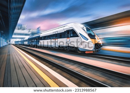 High speed train in motion on the railway station at sunset. Fast moving modern passenger train on railway platform. Railroad with motion blur effect. Commercial transportation. Concept. Travel