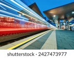 High speed train in motion at the railway station at night. Moving red modern intercity passenger train, railway platform, architecture, city lights. Modern train station in Vienna, Austria. Railroad