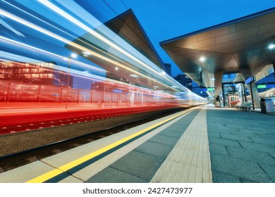 High speed train in motion at the railway station at night. Moving red modern intercity passenger train, railway platform, architecture, city lights. Modern train station in Vienna, Austria. Railroad - Powered by Shutterstock