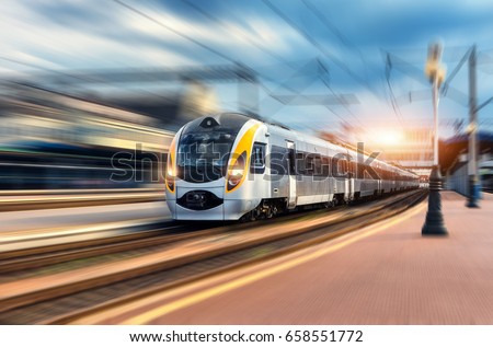 High speed train in motion at the railway station at sunset. Modern european intercity train on the railway platform with motion blur effect. Industrial scene with moving passenger train on railroad
