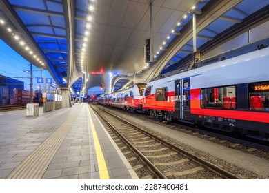 High speed train on the modern railway station at night in Graz, Austria. Beautiful orange intercity passenger train on the covered railway platform with lights. Railroad. Railway transportation - Powered by Shutterstock