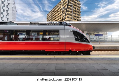 Tren de alta velocidad en la estación de tren al atardecer en Viena, Austria. Hermoso tren rojo moderno de pasajeros en la plataforma ferroviaria, edificios. Vista lateral. Ferrocarril. Transporte comercial