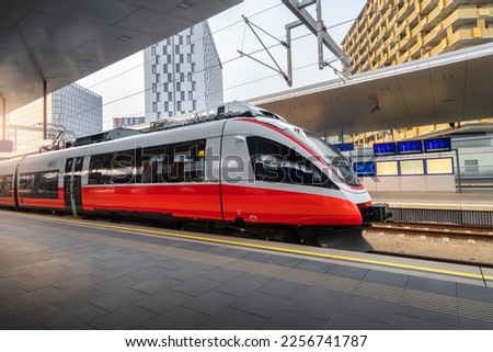 High speed train on the train station at sunset in Vienna, Austria. Beautiful red modern intercity passenger train on the railway platform and buildings. Railroad in Europe. Commercial transportation