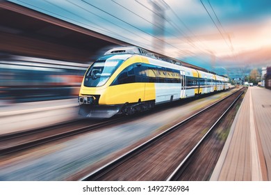 High speed yellow train in motion on the railway station at sunset. Modern intercity passenger train with motion blur effect on the railway platform. Industrial. Railroad and blurred background