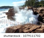 High spray at Thunder Hole, Acadia National Park, Maine, on a sunny day flooding walkway and covering red boulders