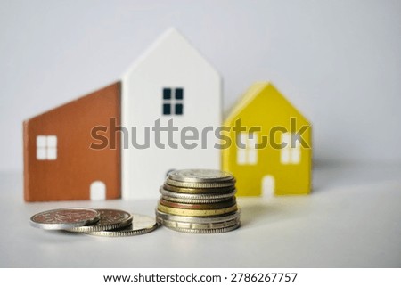 A high stack of coins standing beside three colorful wooden model houses, illustrating substantial real estate savings, compound interest, and strong financial foundations.