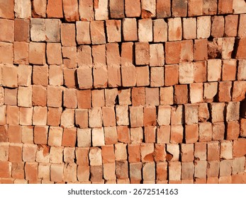 High stack of red bricks arranged in layered pile for construction site storage, traditional Indian building materials in organized bricklaying pattern