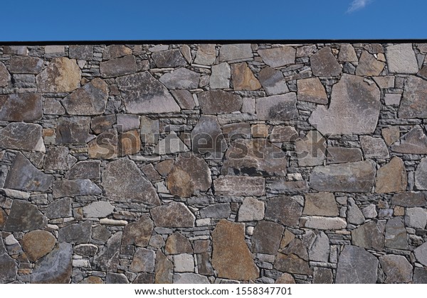 High stone wall in a landscape garden against a clear\
blue sky