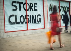 High Street 'Store Closing' Sign With Motion Blurred Shopper Walking Past