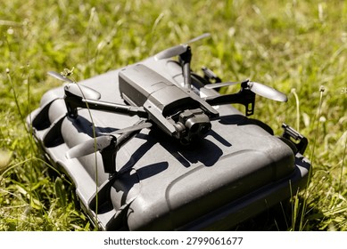 High tech dark grey quadcopter drone with triple camera system standing on a professional hard protective case on green grass