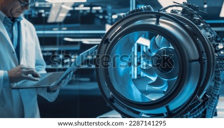 High Tech Prototype Jet Engine in a Technological Startup Facility. Scientist in White Coat Using a Laptop Computer in the Background