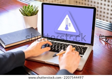 High temperature warning sign on a laptop screen.  Computer overheating concept. Heavy load and hot weather danger. Business office desk background.