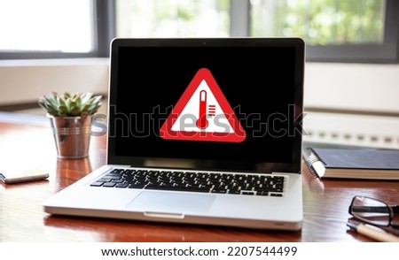 High temperature warning sign on a laptop screen.  Computer overheating concept. Heavy load and hot weather danger. Business office desk background.