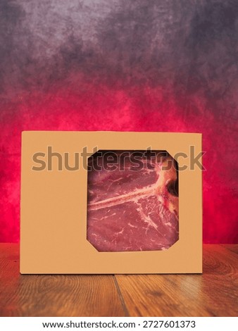High value T bone steak in a brown box is displayed on a wooden board with red burning background. Vacuum packed for freshness top quality beef. Butcher craft and meat industry.