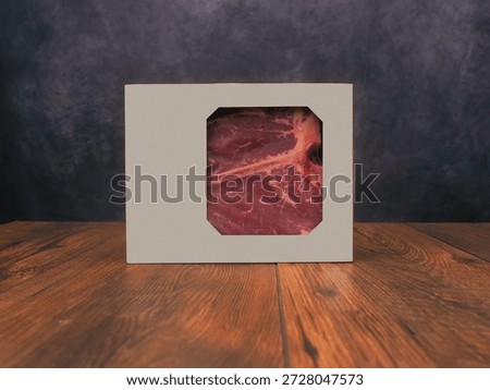 High value T bone steak in a grey box is displayed on a wooden board with dark grey background. Vacuum packed for freshness top quality beef.