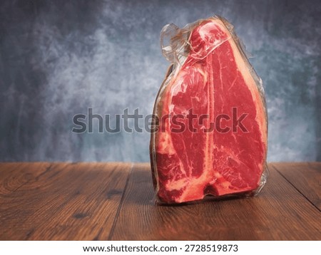 High value T bone steak is displayed on a wooden board with grey classic background. Vacuum packed for freshness top quality beef. Butcher craft and meat industry.