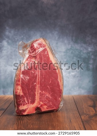 High value T bone steak is displayed on a wooden board with grey classic background. Vacuum packed for freshness top quality beef. Butcher craft and meat industry.
