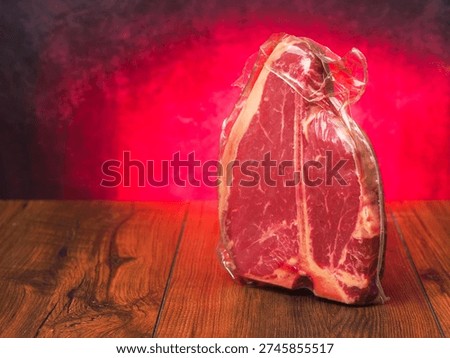 High value T bone steak is displayed on a wooden board with red burning background. Vacuum packed for freshness top quality beef. Butcher craft and meat industry.