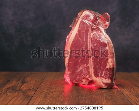 High value T bone steak is displayed on a wooden board with dark background. Vacuum packed for freshness top quality beef. Butcher craft and meat industry.
