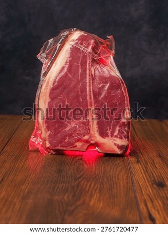 High value T bone steak is displayed on a wooden board with dark background. Vacuum packed for freshness top quality beef. Butcher craft and meat industry.