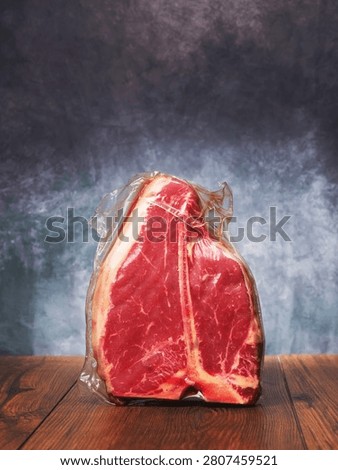 High value T bone steak is displayed on a wooden board with grey classic background. Vacuum packed for freshness top quality beef. Butcher craft and meat industry.