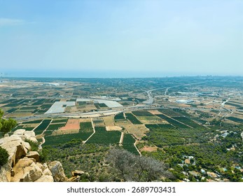 From a high vantage point, a sprawling patchwork of green and brown fields stretches toward the horizon, meeting the shimmering sea.