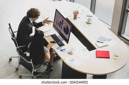High view of caucasian marketing professional couple sit together at office desk with paper of creative idea and computer screen to discuss business account and portfolio chart to design work strategy