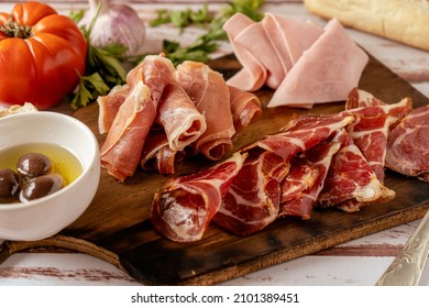 High View Of A Delicious Table Of Serrano Ham, Cooked Ham And Pickled Pork Butt Accompanied With Black Olives. Appetizer Concept, Animal Protein.