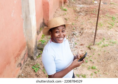 High View Image Of A Pretty Young Black Female Entrepreneur Sending Text With Phone Whilst Looking At Camera