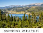 A high view looking down onto Dillon Reservoir.  Blue water and blue sky with mountain scenes. Overlook of Lake Dillon with town of Keystone on shoreline.