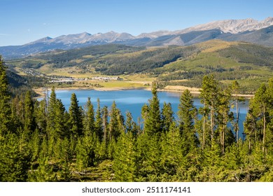 A high view looking down onto Dillon Reservoir.  Blue water and blue sky with mountain scenes. Overlook of Lake Dillon with town of Keystone on shoreline.