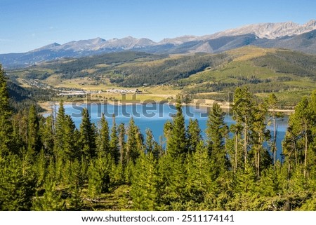 A high view looking down onto Dillon Reservoir.  Blue water and blue sky with mountain scenes. Overlook of Lake Dillon with town of Keystone on shoreline.