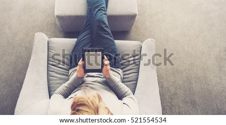 High view of a young blond man reading a book on digital device