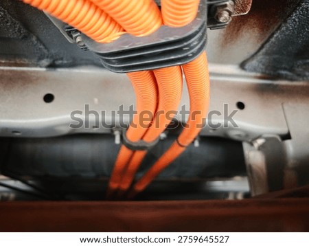 High voltage electrical cable of an electric vehicle shown during maintenance inspection at automotive service center. The image represents EV battery technology, electric mobility infrastructure and modern automotive engineering.