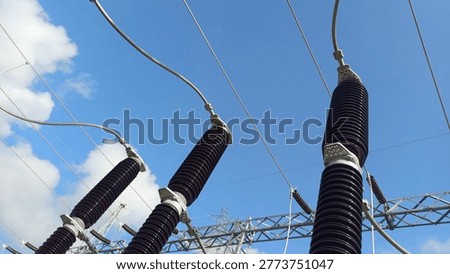 High voltage electrical insulators at a power substation against a blue sky. Industrial electricity transmission equipment and porcelain bushings in a distribution network providing energy for urban infrastructure.