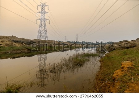 High voltage Electrical power lines supplying electricity to Purulia, West Bengal, India. Sky background and waterbody foreground.