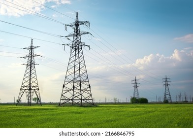 High voltage lines and power pylons in a flat and green agricultural landscape on a sunny day with clouds in the blue sky. Cloudy and rainy. Wheat is growing