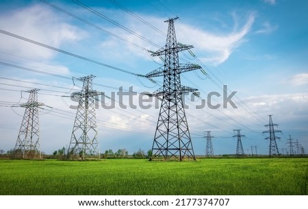 High voltage lines and power pylons in a flat and green agricultural landscape on a sunny day with clouds in the blue sky. Cloudy and rainy. Wheat is growing