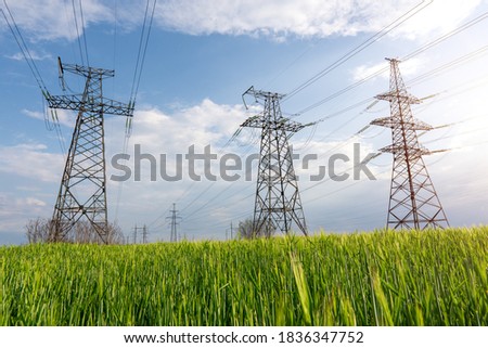 High voltage lines and pylons and a green agricultural landscape on a sunny day. Association of agriculture and industry in one photo. Beautiful spring landscape of the European plain.