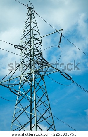 High voltage metal tower supporting power lines with blue sky and white clouds