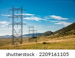 High voltage power line on open grassy plain with steel pylon next to Dakota Hogback against blue sky with white cirrus clouds