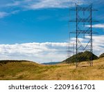 High voltage power line on open grassy plain with steel pylon next to Dakota Hogback against blue sky with white stratus clouds